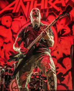 an image of a man that is playing guitar in front of some red lights on the stage