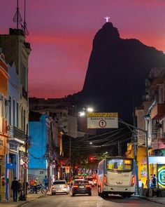 a city street at night with cars and people on the side walk, mountains in the background