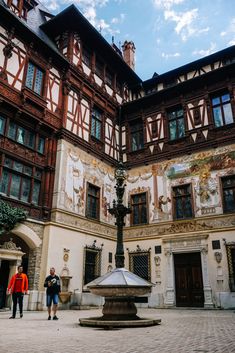 two people are standing in front of a building with an ornately painted facade and fountain