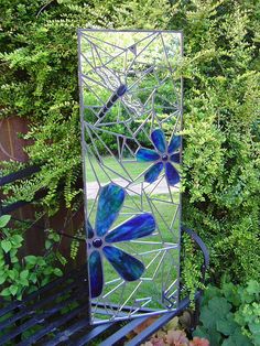 a mirror sitting on top of a metal bench in front of some bushes and trees