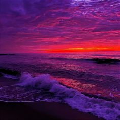 the sun is setting over the ocean with waves coming in to shore and purple clouds