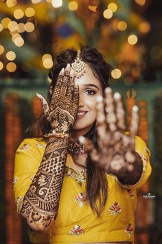 a woman in yellow holding her hands up to show the henna on her hand