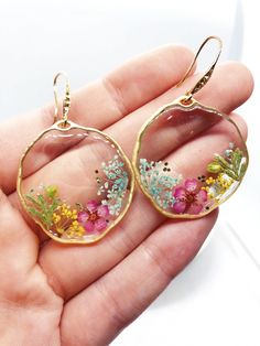 a hand holding a pair of earrings with flowers in it's glass cabochons