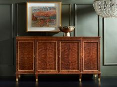 a wooden cabinet sitting in front of a painting on the wall next to a chandelier