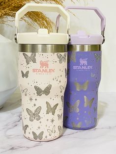 two stainless steel insulated tumblers with butterfly designs on them, one is purple and the other is white