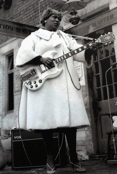 a man playing guitar in front of a building with an old fashioned microphone and amp