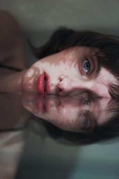 a woman with freckles on her face is reflected in the water