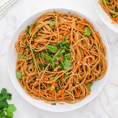 two white bowls filled with noodles and carrots on top of a marble countertop