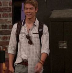 the young man is smiling while standing in front of a brick wall and wearing a backpack