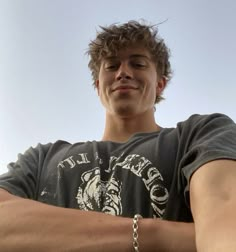 a young man with his arms crossed holding a frisbee in one hand and wearing a chain bracelet on the other