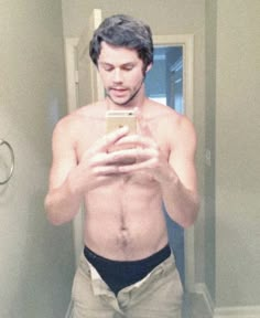 a shirtless man taking a selfie in the mirror with his cell phone,