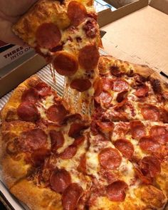 a pepperoni pizza being lifted from a box by a person holding a spatula