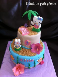 a hello kitty birthday cake on top of a purple tablecloth with pink flowers and palm trees