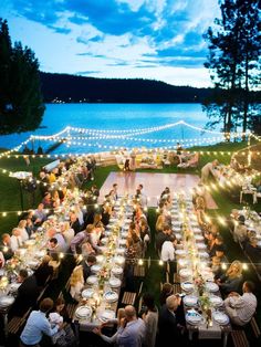 an outdoor dinner is set up on the lawn by the water at night with string lights