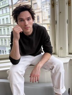 a man is sitting on a window sill with his hand up to his face