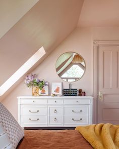 a white dresser sitting under a window next to a bed