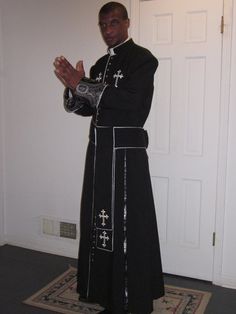 a man in a priest's outfit standing with his hands folded