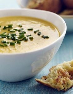 a white bowl filled with soup next to bread on a blue tablecloth and two plates