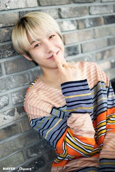 a person leaning against a brick wall with their hand on her chin and looking at the camera