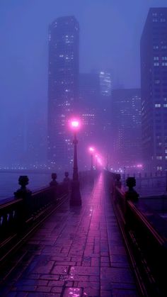 a foggy city street at night with the lights on and buildings in the background