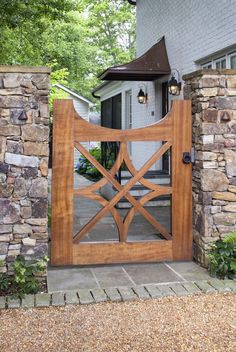 a large wooden gate in front of a house with stone walls and trees around it