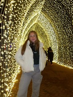 a woman standing in front of a tunnel covered with lights