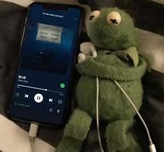 a green stuffed animal laying on top of a bed next to an mp3 player