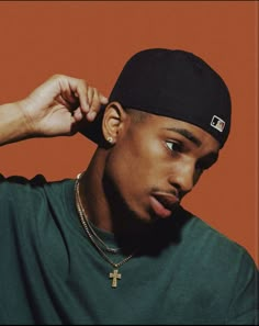 a young man wearing a black hat and green shirt with a cross on the front