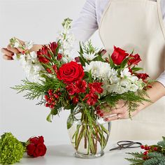 a woman in an apron holding a vase filled with red roses and white carnations