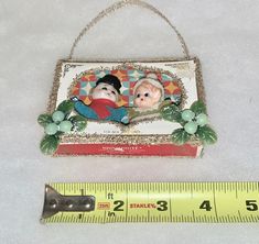 an ornament with two small dolls on it next to a ruler