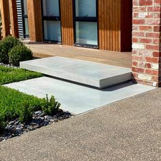 a concrete bench sitting in front of a brick building next to green grass and bushes