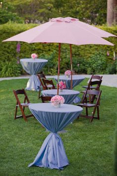 an outdoor table set up with blue linens and pink flowers on the tables under an umbrella