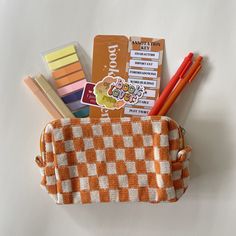 an orange and white checkered purse with pens, pencils, and other items