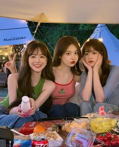 three young women sitting next to each other at a table covered in food and drinks