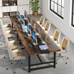 a long table with several computers on it in an office setting, surrounded by chairs and potted plants