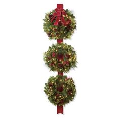 three christmas wreaths hanging on a pole with red bows and lights around the top