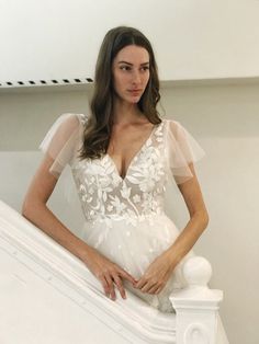 a woman standing on top of a white stair case wearing a wedding dress with sheer sleeves