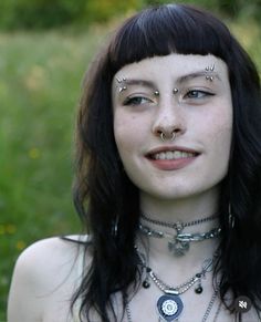 a woman with piercings on her nose and chest is posing for a photo in the grass