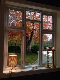 an open window with candles on the windowsill in front of it and trees outside