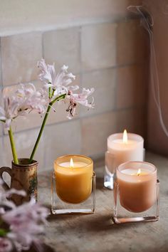 three candles sitting on top of a table next to a vase with flowers in it