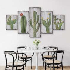 a table with four chairs and three cactus paintings on the wall