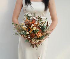 a woman in a white dress holding a bouquet of flowers and greenery on her wedding day