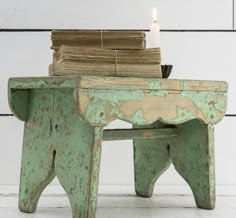 an old green bench with a lit candle on it and stack of books sitting on top