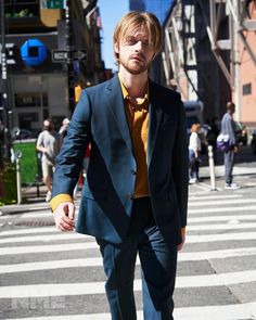 a man in a blue suit and yellow shirt crossing the street at a crosswalk