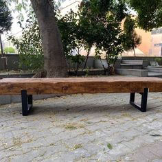 a large wooden bench sitting on top of a stone floor next to a tree in a park