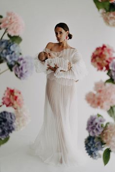 a woman holding a baby in her arms and wearing a dress with ruffles