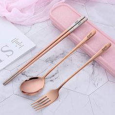 three forks and two spoons in a pink case on a marble countertop next to a book