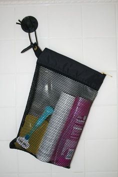 a black mesh bag hanging on the wall next to a white tiled wall with various items in it