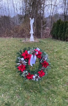 a wreath with poinsettis and pine cones on the grass in front of a statue