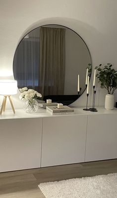 a large round mirror sitting on top of a white dresser next to a vase filled with flowers